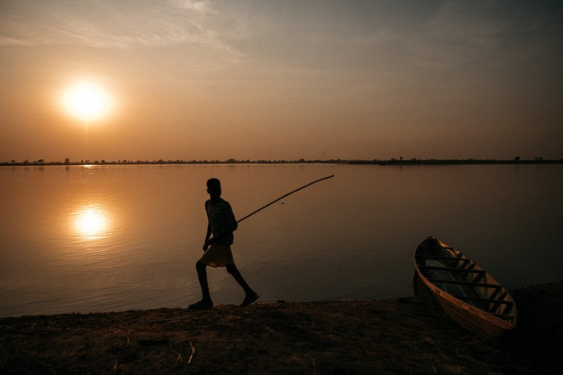 Atardecer en un lago en Chad, un niño con una pértiga y una canoa de madera