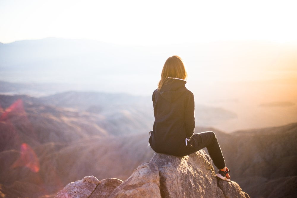 Mujer joven viendo el atardecer en lo alto de una cima de una montaña 