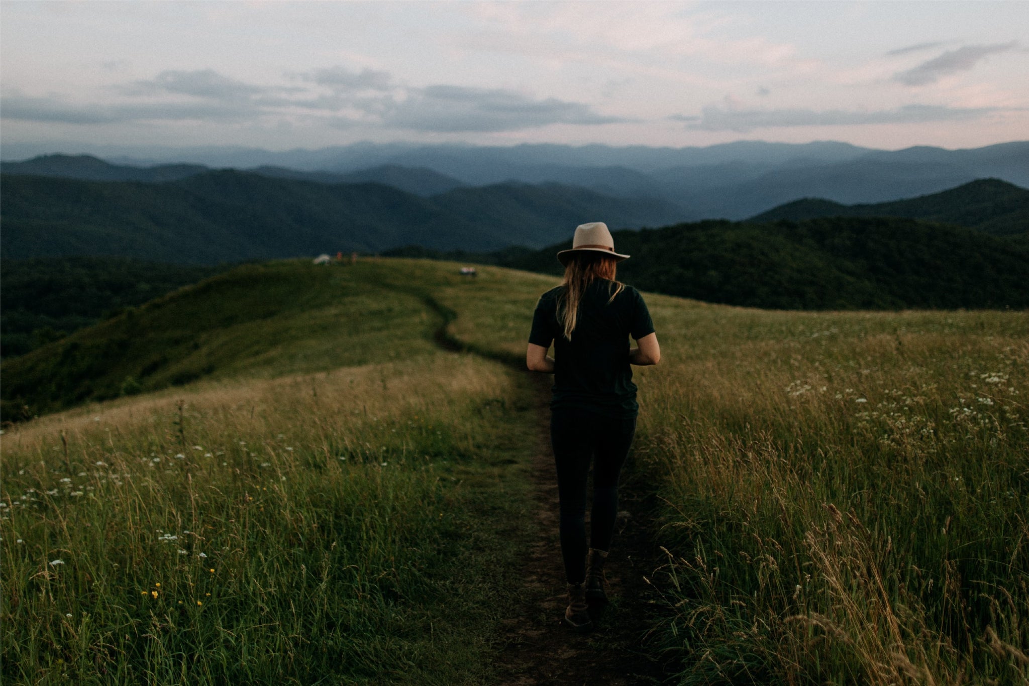 Paisaje verde con montañas al fondo y una mujer con sombrero de espaldad