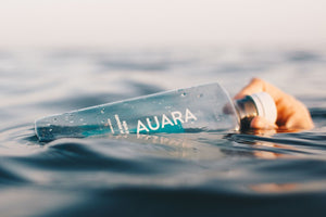 Botella de AUARA en el agua sujeta por una mano.