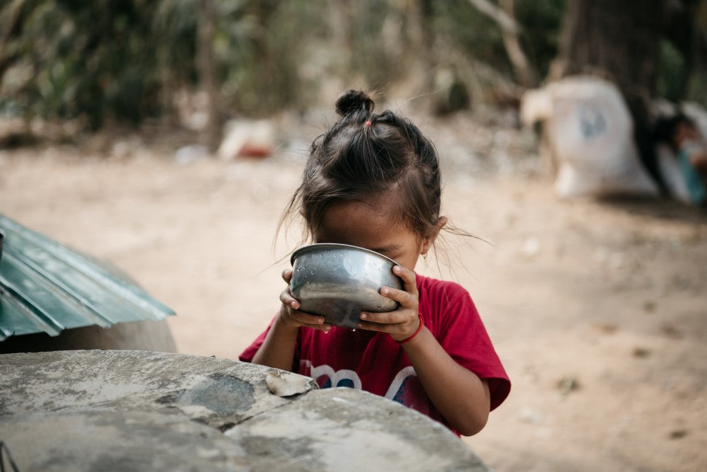Niña pequeña beneficiaria de un proyecto de AUARA en Camboya bebiendo agua de un recipiente metálico