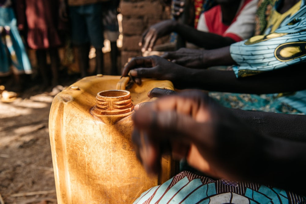 Primer plano de varias manos junto a un JerryCan en Chad